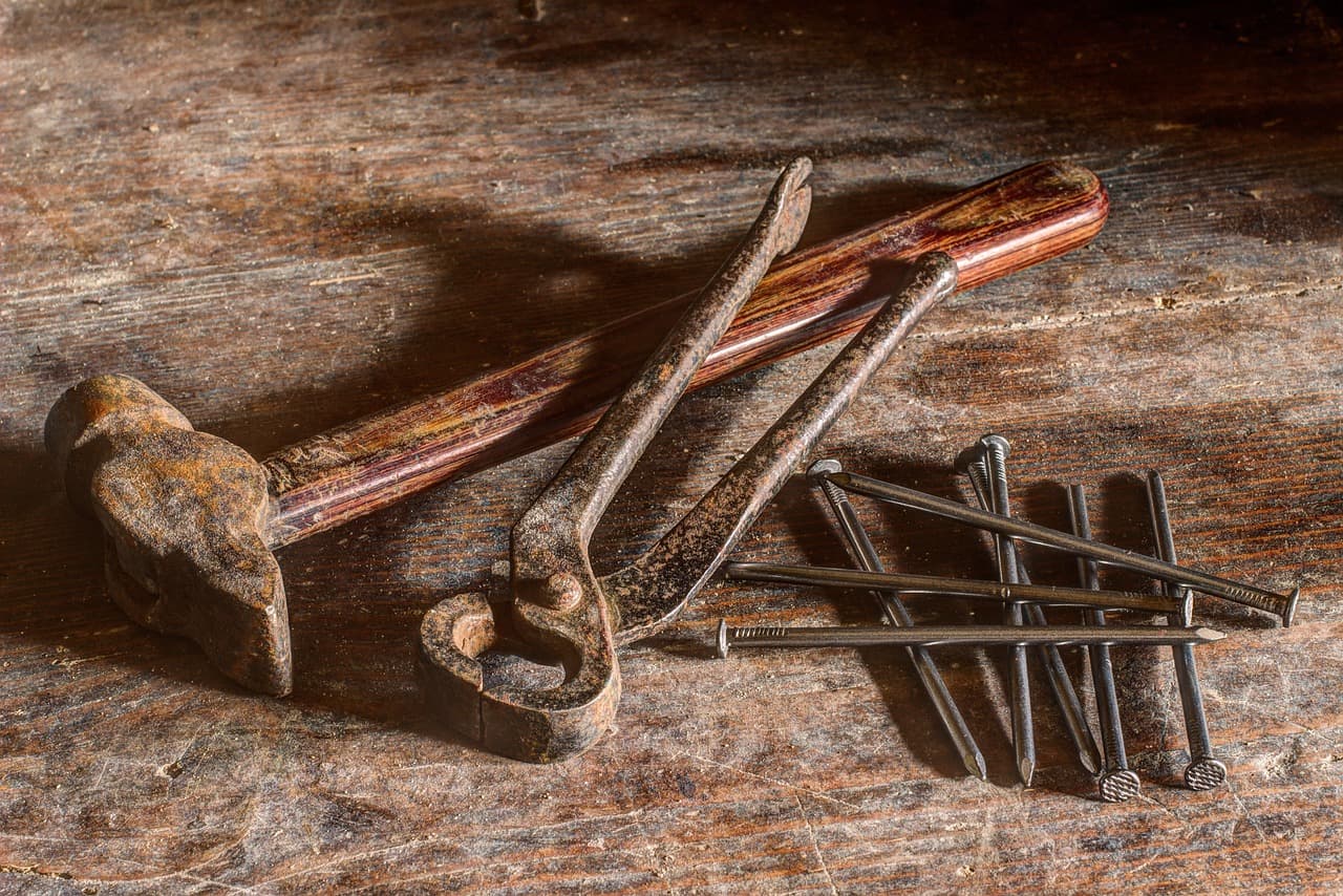 An old hammer, pliers and nails on a worn wooden bench