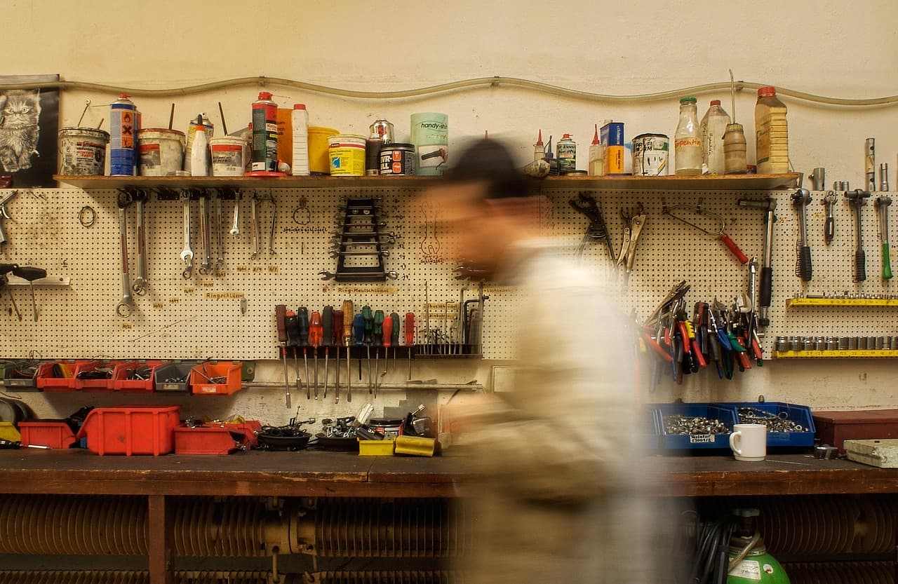 A workshop wall of tools and parts, a mechanic passing the bench